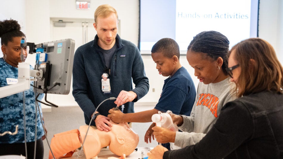 A UVA Doctor encourages health career interest with local students as he demonstrates placing a line with a mannequin.