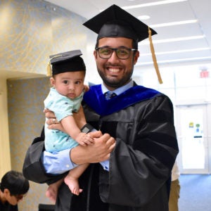 Student in cap in gown with baby in small graduation cap