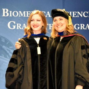 Student smiling as she stands on the stage with faculty