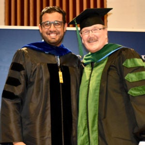 Student smiling as he receives diploma with faculty