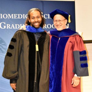 Student smiling as he receives diploma from faculty