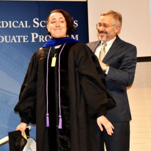 Student smiling as she walks across the stage with faculty