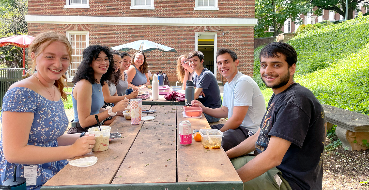Students at picnic table for class lunch break facing camera and smiling.