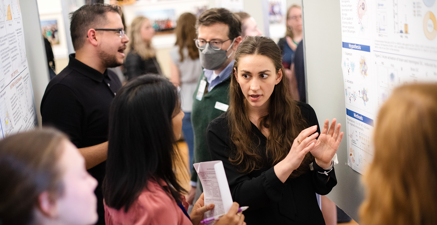 Students discussing posters at the 2023 GBS Symposium. Several students talking and gesturing with scientific posters in the background.