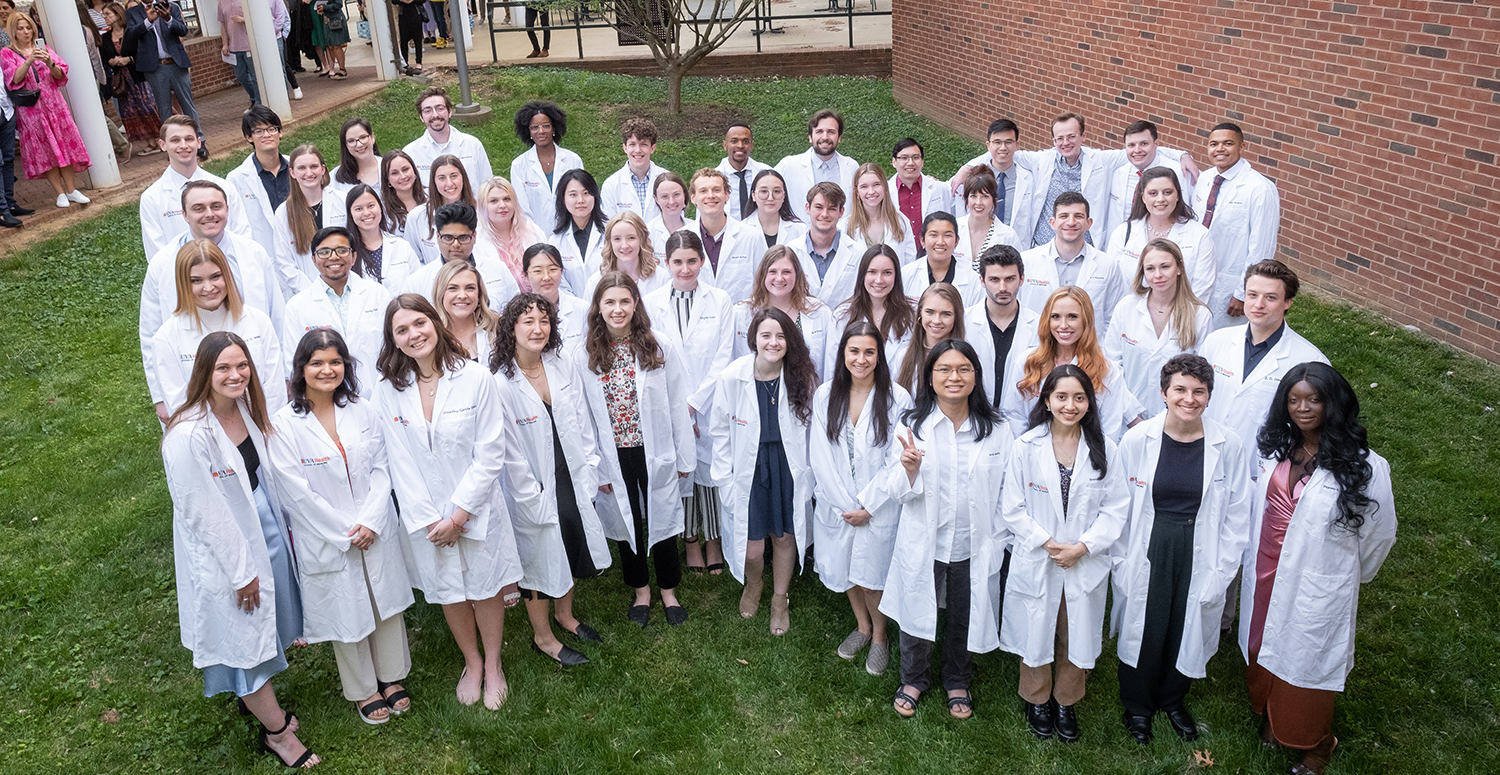 Group of students wearing personalized embroidered lab coats, looking up at camera.