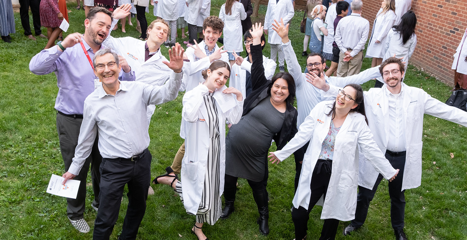 students in white coats and faculty posing silly after ceremony