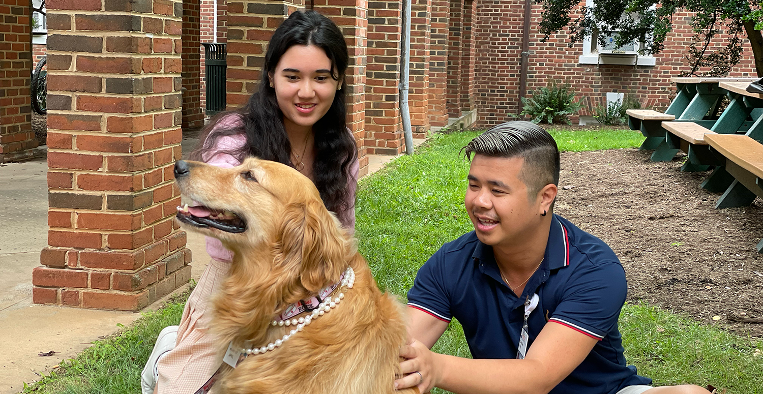 Two students sitting with a therapy dog who is visiting for an exam break.
