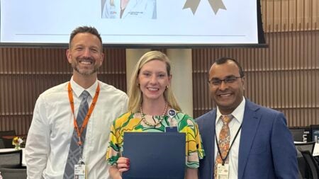Three people standing together, person in center showing an award certificate