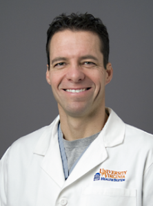 Dr. John Riordan smiling at the camera while wearing a white coat