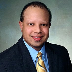Sanjay Kripalani looking at the camera while wearing a dark suite, blue dress shirt, and yellow tie