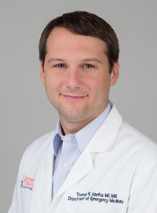 Dr. Thomas Hartka smiles at the camera while wearing his white physician coat