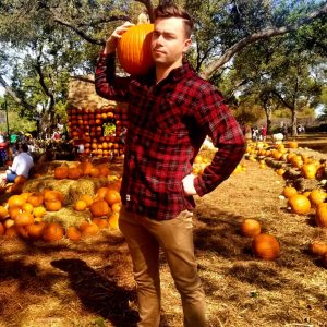 Jackson holding a pumpkin on his shoulder while standing in a pumpkin patch