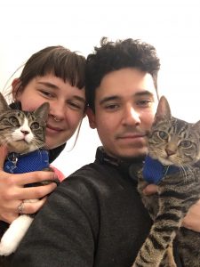 A couple looking at the camera holding cats
