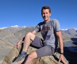 Nate East smiling and sitting on a rock in front of mountains