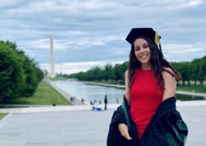 portrait of Angelica Rego in her graduate regalia in front of the Washington Monument and reflection pool in Washington, DC