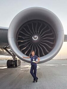 Doctor Sara Sutherland stands in scrubs in front of a large airplane engine