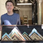Matthew holding a panoramic wood project that is a framed mountain image