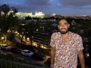 Pedro at an overlook after dark with a city and a lighted building in the background