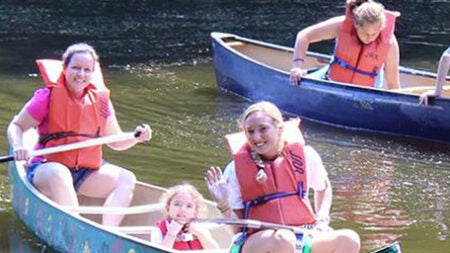 Three girls in a canoe wearing life jackets and smiling
