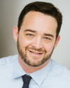 Brant Isakson smiles in a headshot while wearing a white shirt