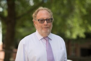 Mark Kester poses in front of greenery, wearing a tie and glasses