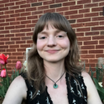 Graduate Student Mary MacMillan Smiles in front of a brick wall