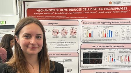 Kasia smiles and stands in front of her science poster