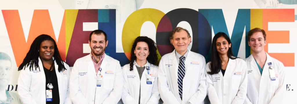 UVA Radiology's Diversity and Inclusion representatives pose with Dr. Juliana Bueno and Dr. Eduard de Lange in front of the welcome sign the main hospital lobby