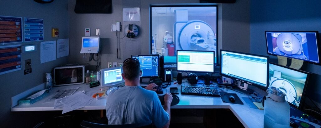An MRI technologist images a patient from the adjacent control room