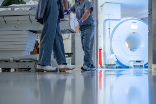 MRI technologists wheel a patient into a scanner room on a stretcher.