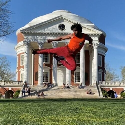 UVA Radiology resident Dr. Xavier Mohammed does a kick high in the air in front of the UVA Rotunda