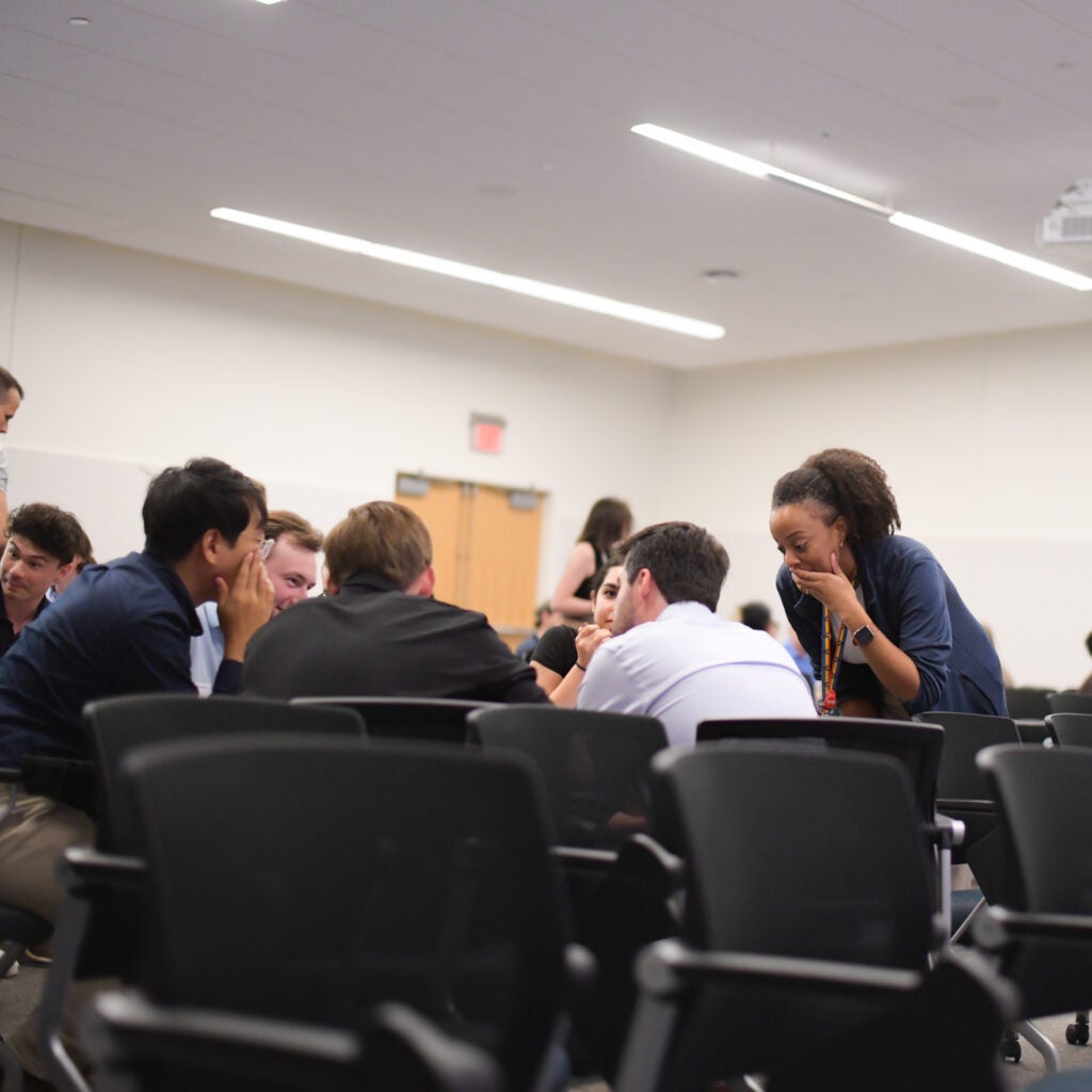Group of 5 students in a discussion group as an IR trainee looks on and supervises