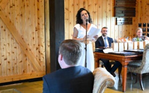 Juliana Bueno, MD speaks at a microphone as Joe Donahue, MD and Carrie Rochman, MD look on from the background