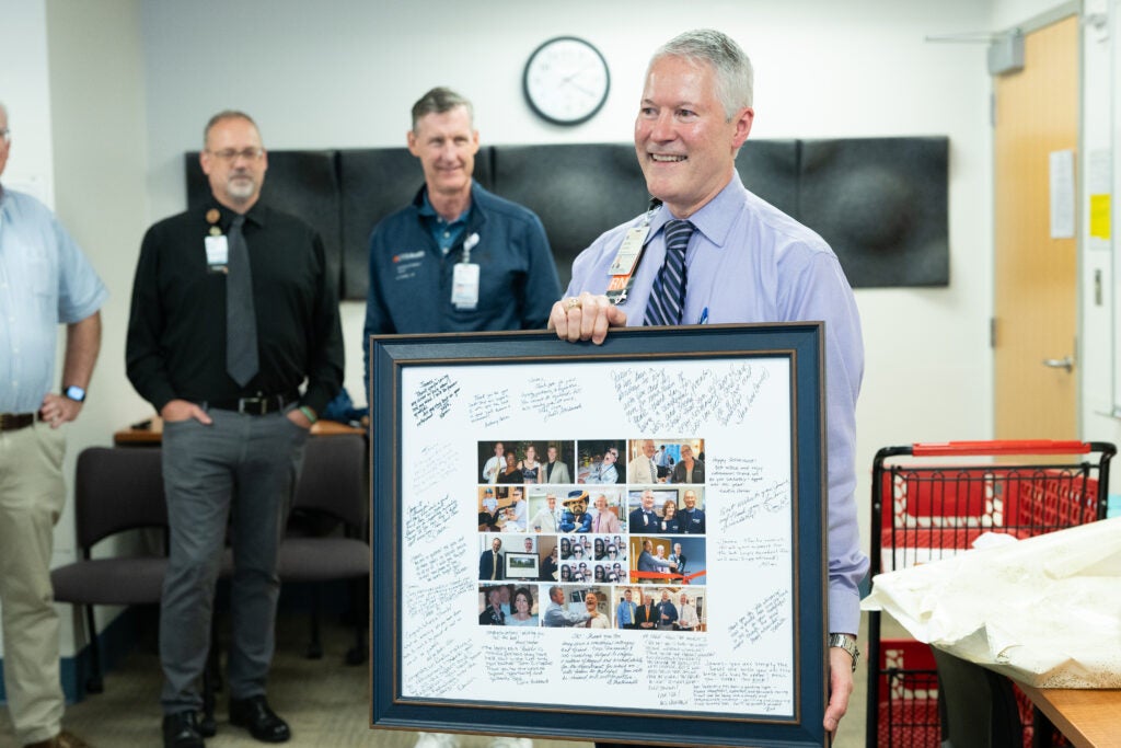 James Carnes stands with framed photo collage with onlookers
