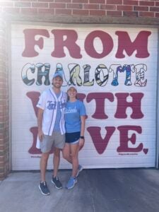 Kristen Reeder and partner in front of sign reading "From Charlotte with Love"