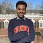 A man stands outside on UVA's grounds in a blue sweater