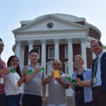 a group of people stand in front of the UVA rotunda with a gold plaque and green liquid. 