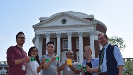 a group of people stand in front of the UVA rotunda with a gold plaque and green liquid.